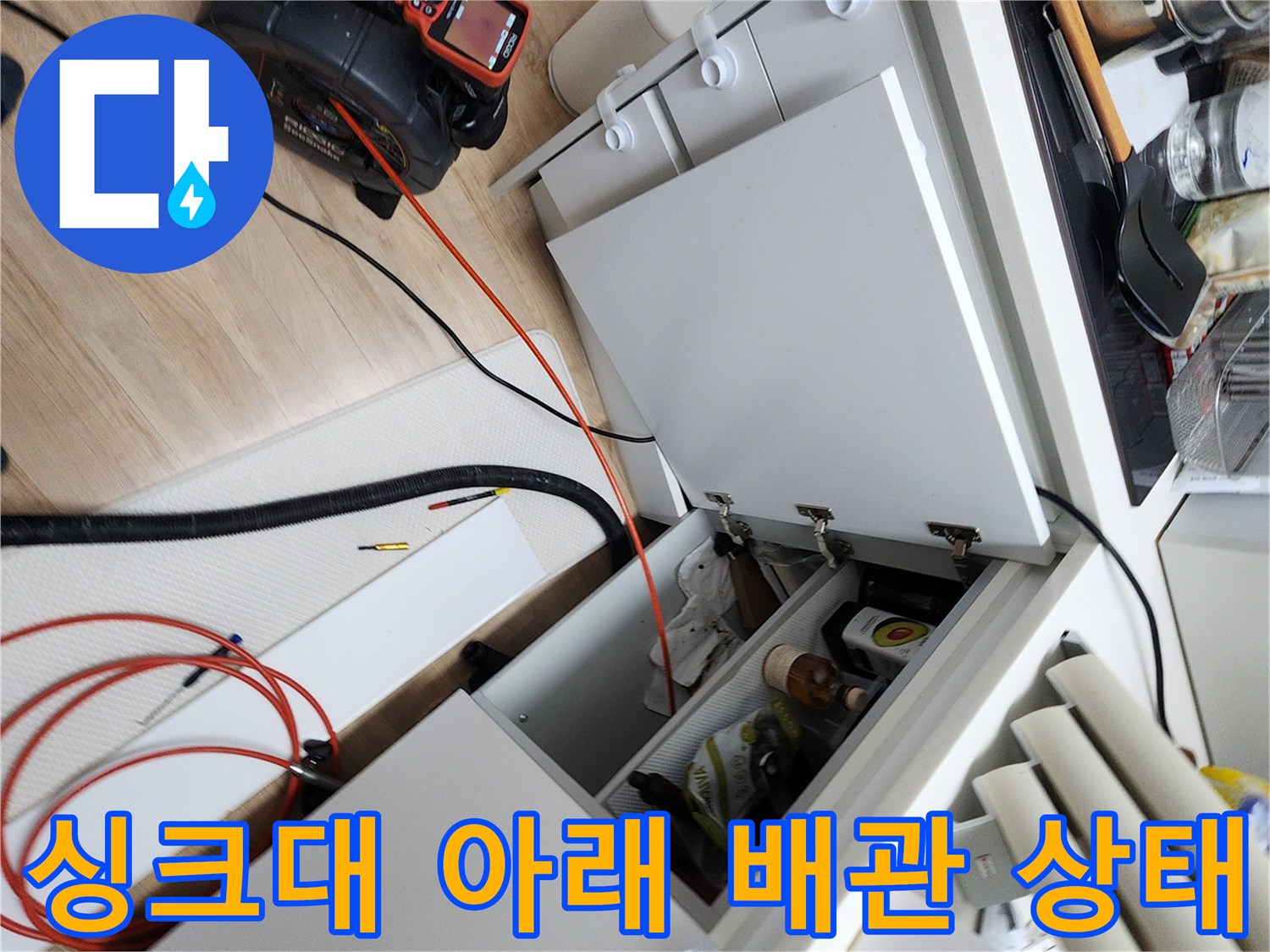 싱크대 하부장 내부의 붉은색 배관과 내시경 장비가 놓인 현장 사진