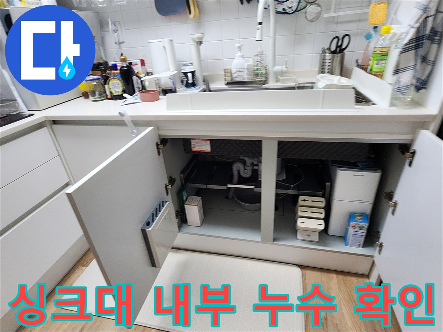싱크대 하부장 문을 열고 바닥 배관 부위를 정밀하게 조사하는 장면입니다.