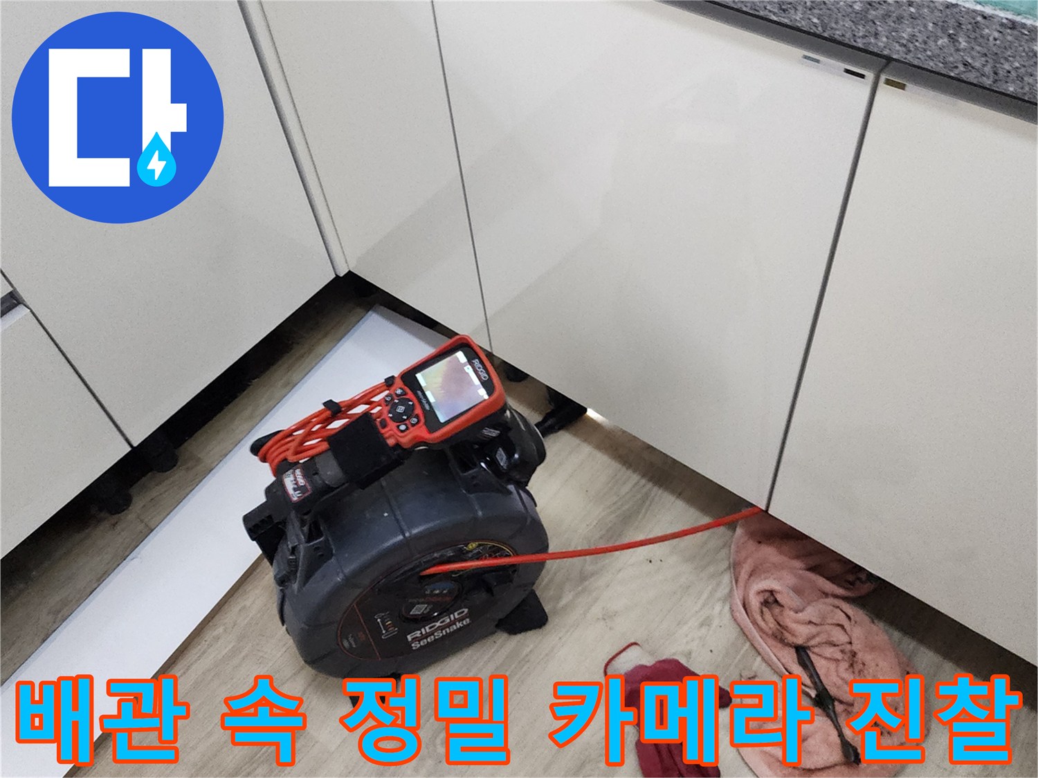 주방 가구 아래 좁은 공간에서 진행되는 배관 내시검사 작업 현장