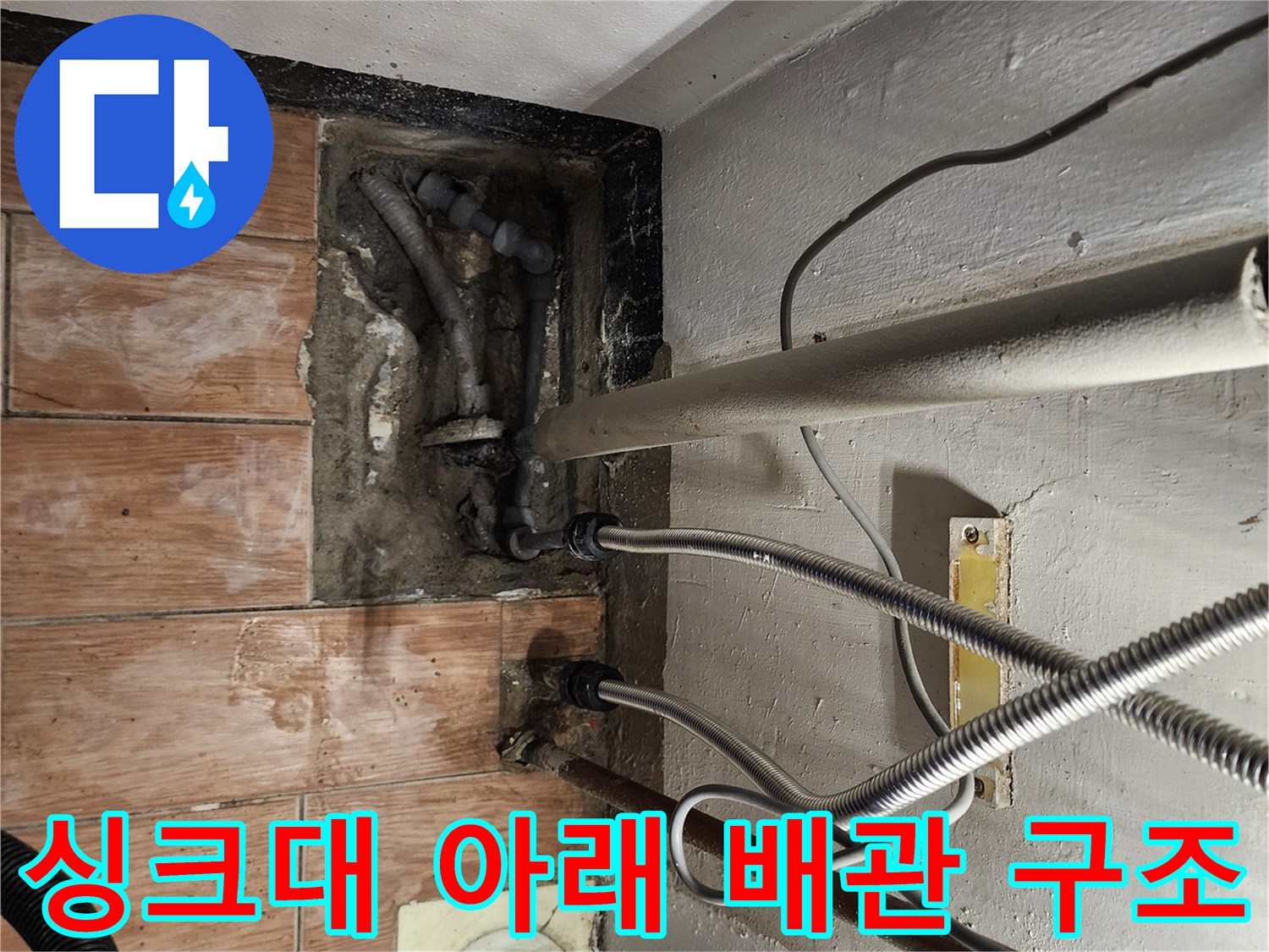 주방 싱크대 하부의 은색 호스와 수직 배수관 연결 부위