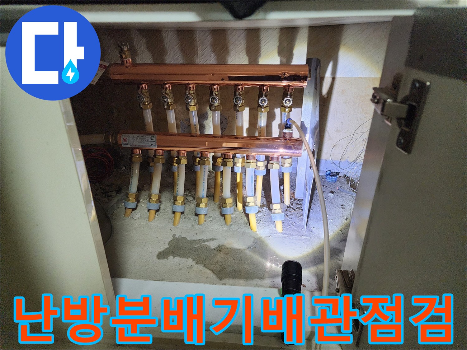 싱크대 하단 공간에 노출된 난방 분배기 및 연결 배관의 근접 촬영