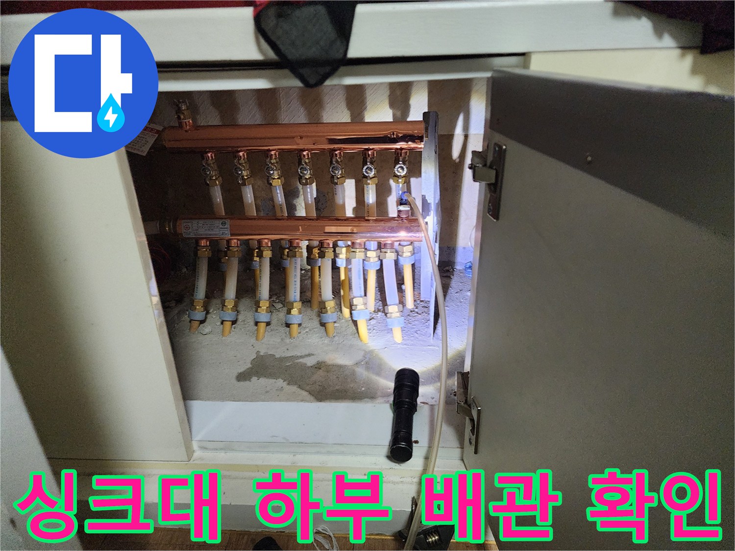 싱크대 하단에 노출된 구리 색상의 분배기와 다수의 연결 배관들입니다.