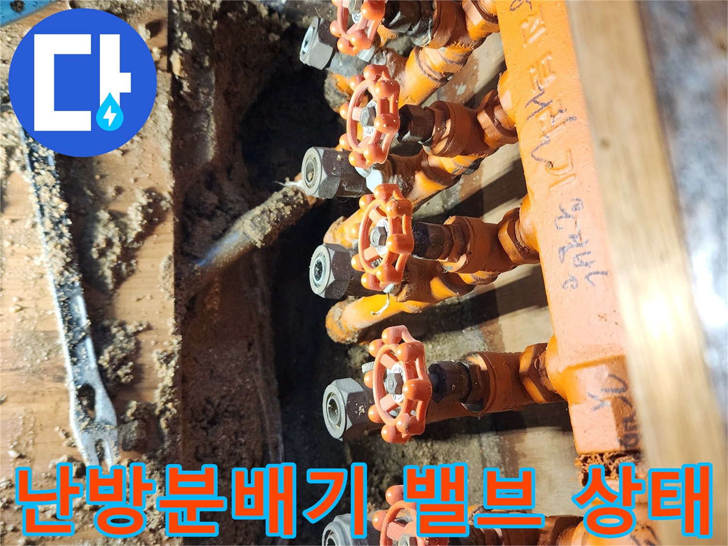 주방 싱크대 하부장 내부 - 오렌지색 보온재로 감싸진 난방 분배기 밸브 부위