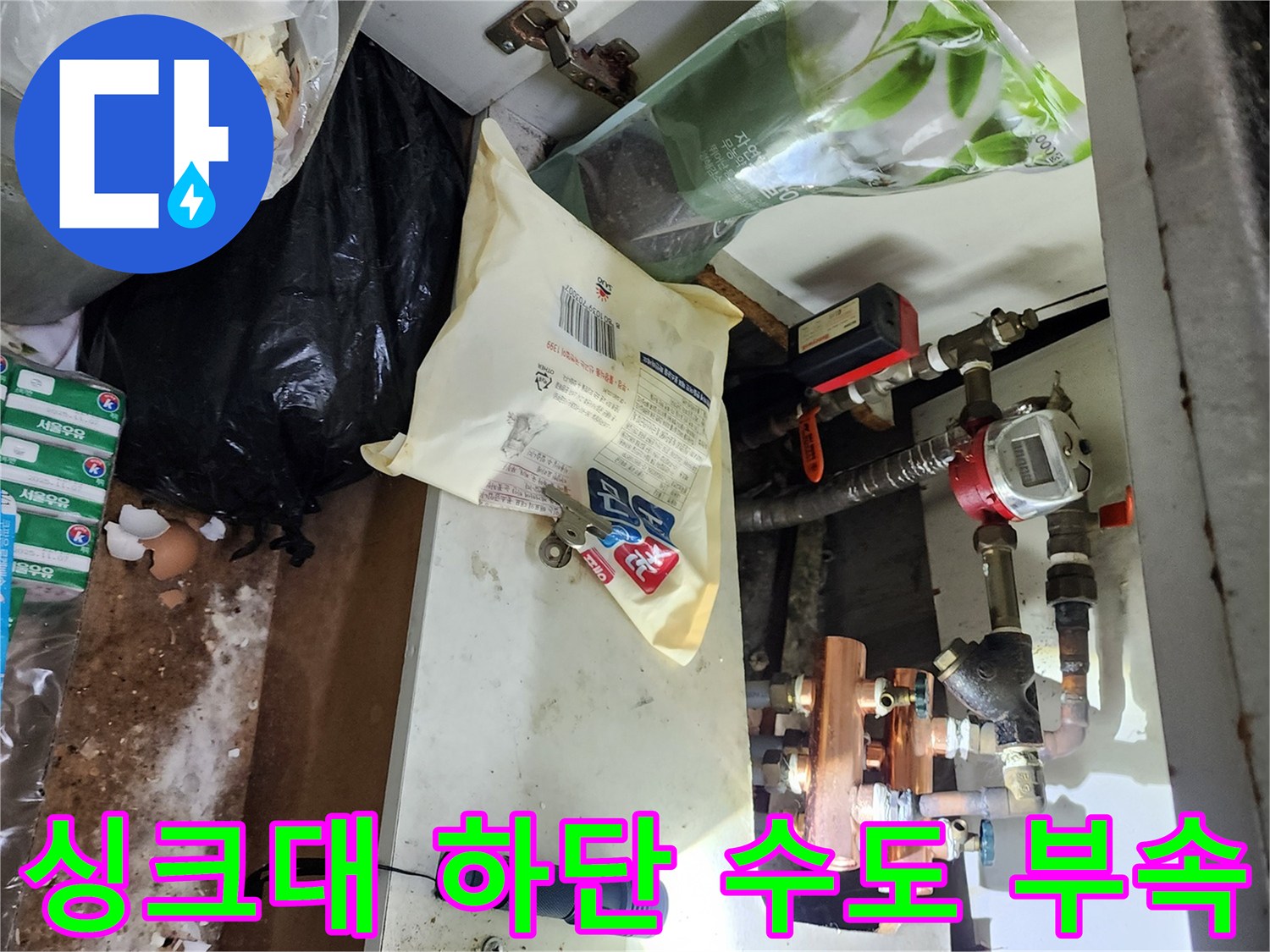 어두운 싱크대 하부장 안쪽의 배관과 연결 부품 모습