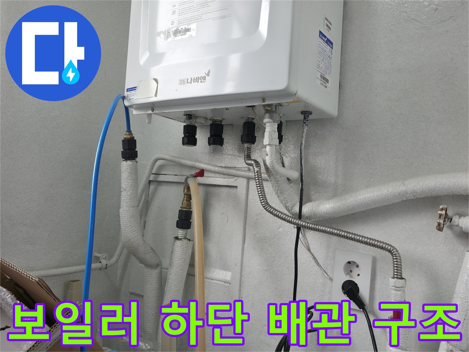 보일러 본체 아래 연결된 파란색 호스와 은색 주름관의 모습입니다.