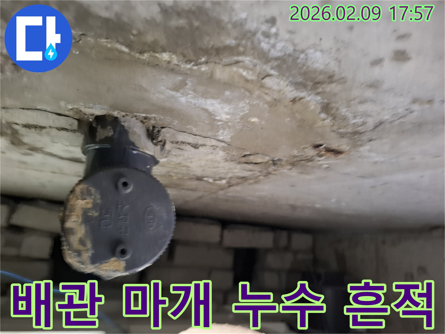 천장 배관의 마개 주변에서-발견된-오래된 누수 흔적과-콘크리트 손상을-보여주는-이미지입니다.