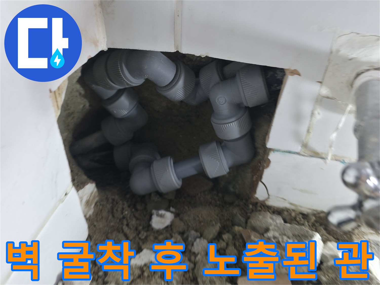 타일 뒤편에 드러난 회색 수도 연결 배관과 파쇄된 벽면