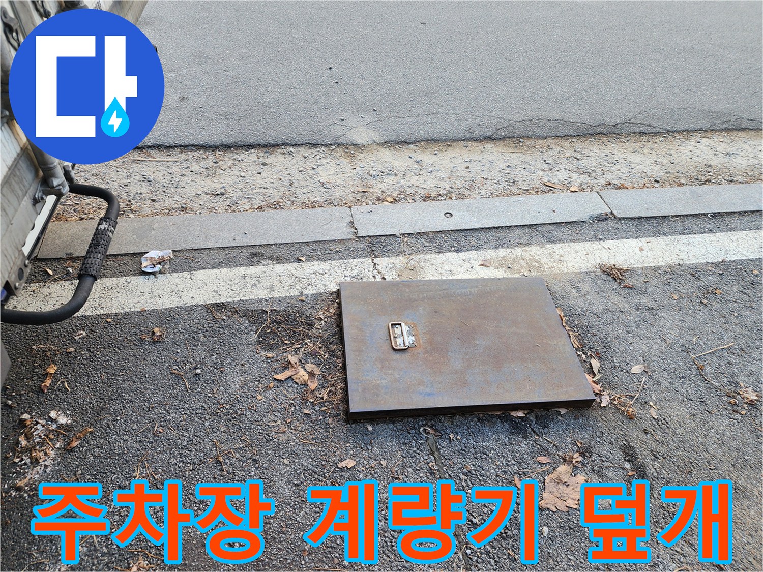 주차장 바닥에 설치된 금속 재질의 수도 계량기 함 덮개 모습입니다.