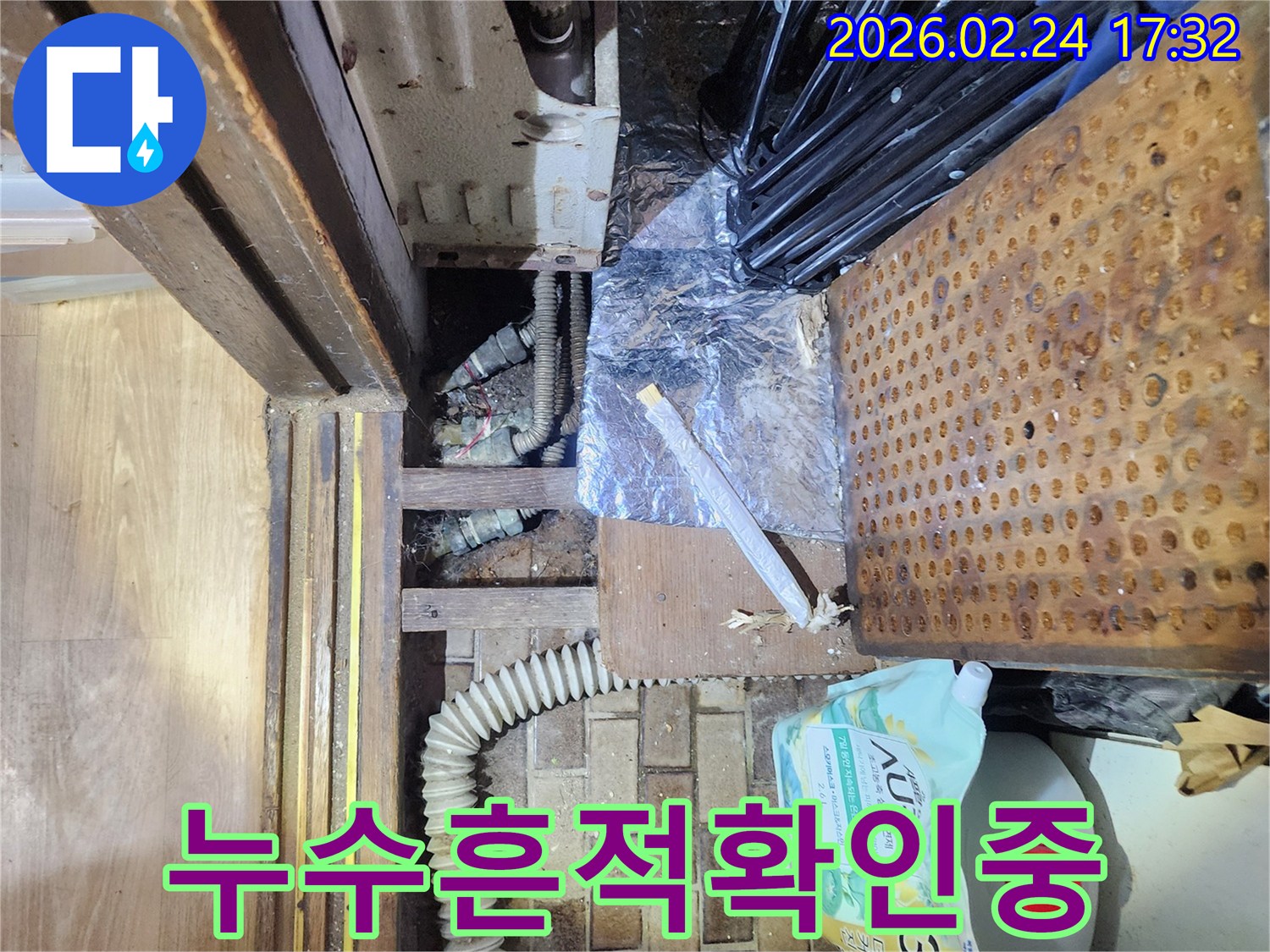 물건들로 가득 찬-좁은 공간 아래에서-누수 지점을 찾아내기 위해-조사하는 장면입니다