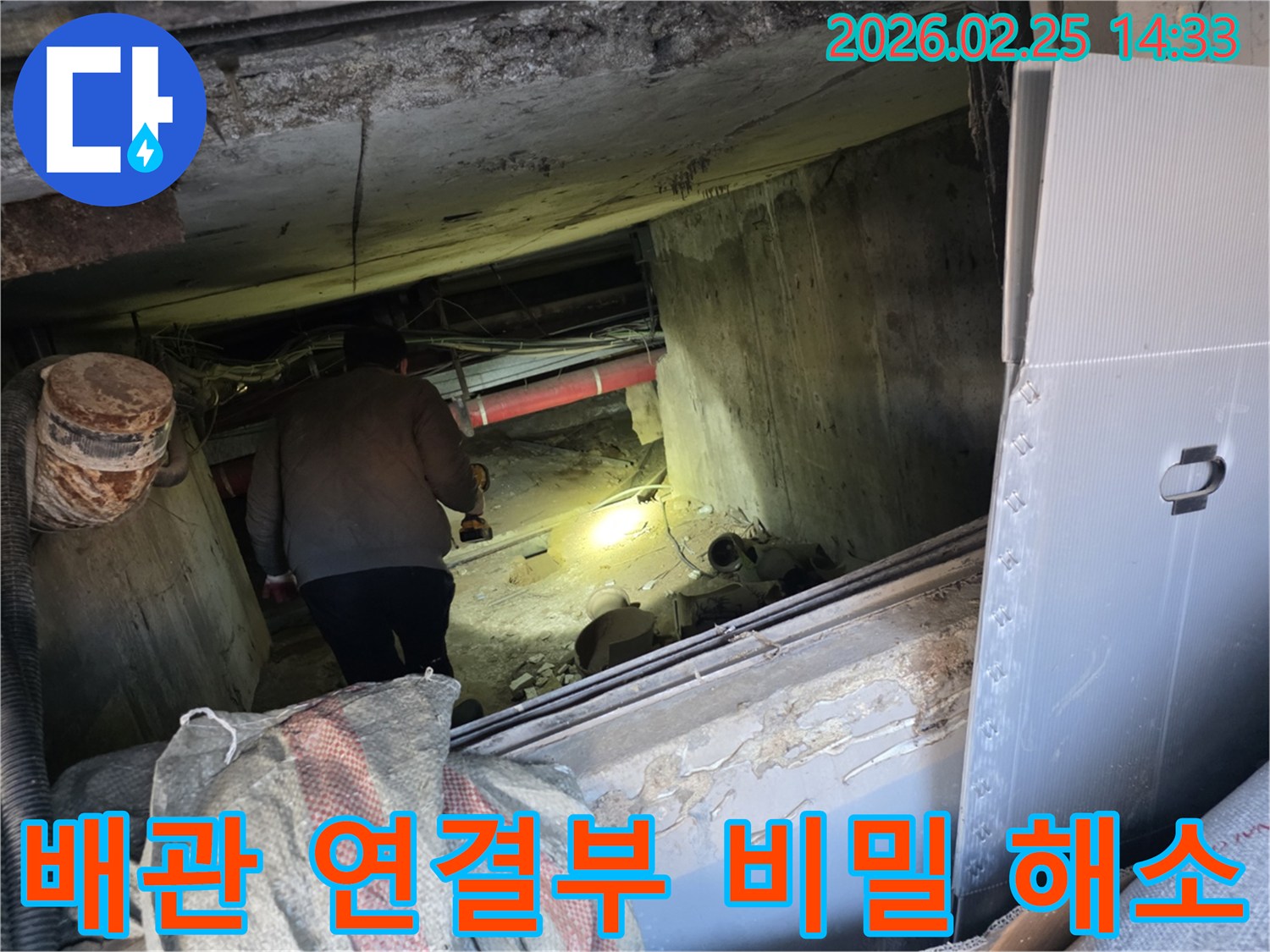 누수 전문 엔지니어가-어둡고 좁은 공간에서-손전등을 비춰가며-배관 연결부의 숨겨진 누수 여부를-정밀하게 점검하는 모습입니다.