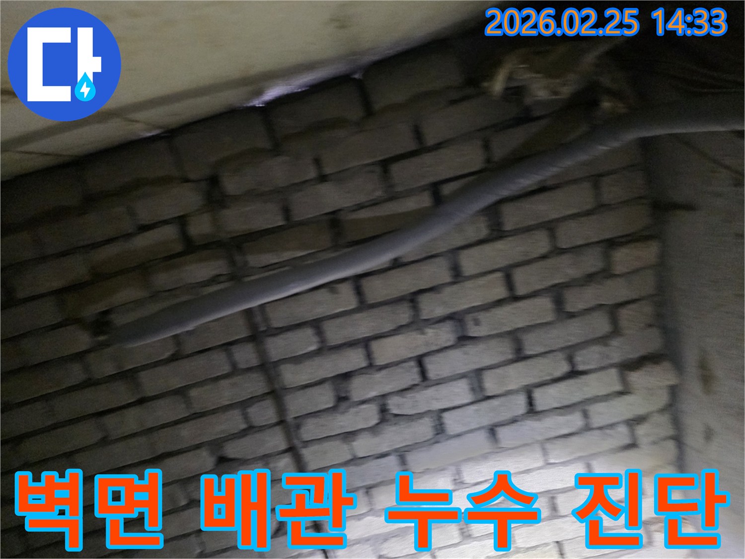 어두운 벽돌 벽면을 배경으로-단열재로 감싸인 배관과-다른 배선이 누수 여부를-확인하기 위해 촬영된 현장 이미지입니다.
