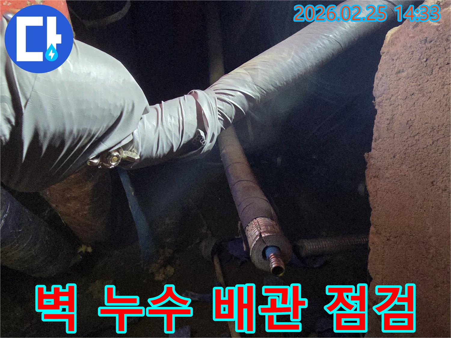 어두운 벽체 내부에서-장갑을 낀 손이-손상된 배관의-연결 부위를-세심하게 점검하며-누수 원인을-확인하는 모습입니다