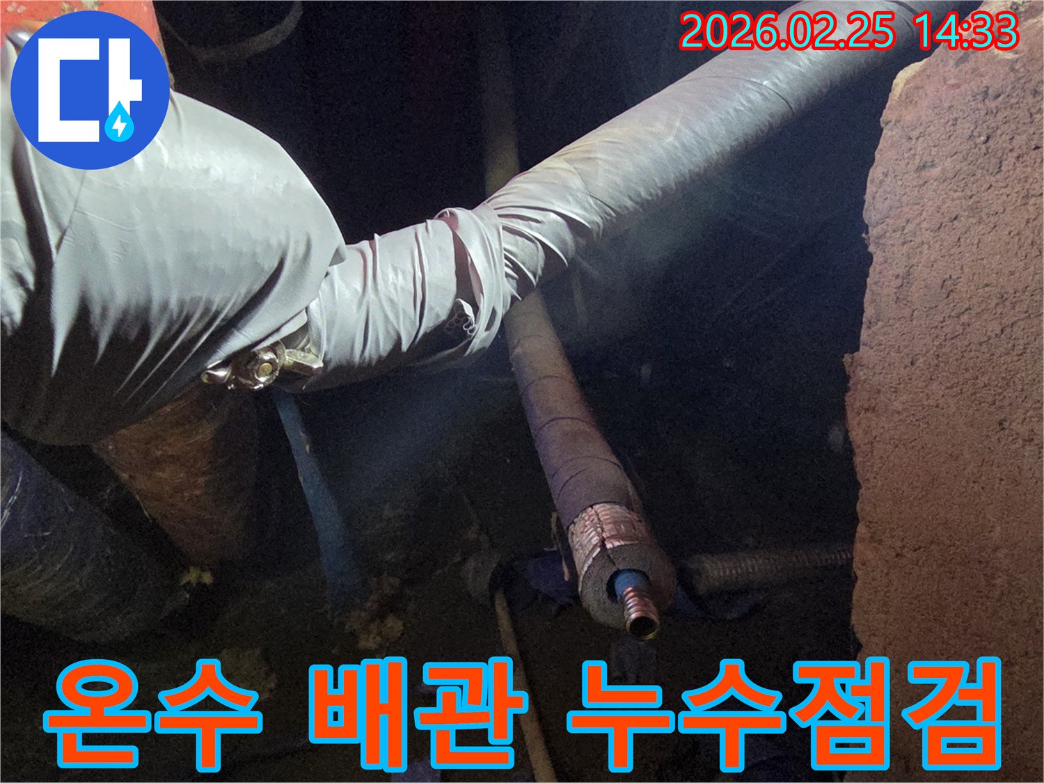 어두운 작업 공간에서-장갑을 낀 손이-뜨거운 온수 배관의-손상된 연결 부위를-세심하게 점검하며-누수 지점을-확인하는 모습입니다