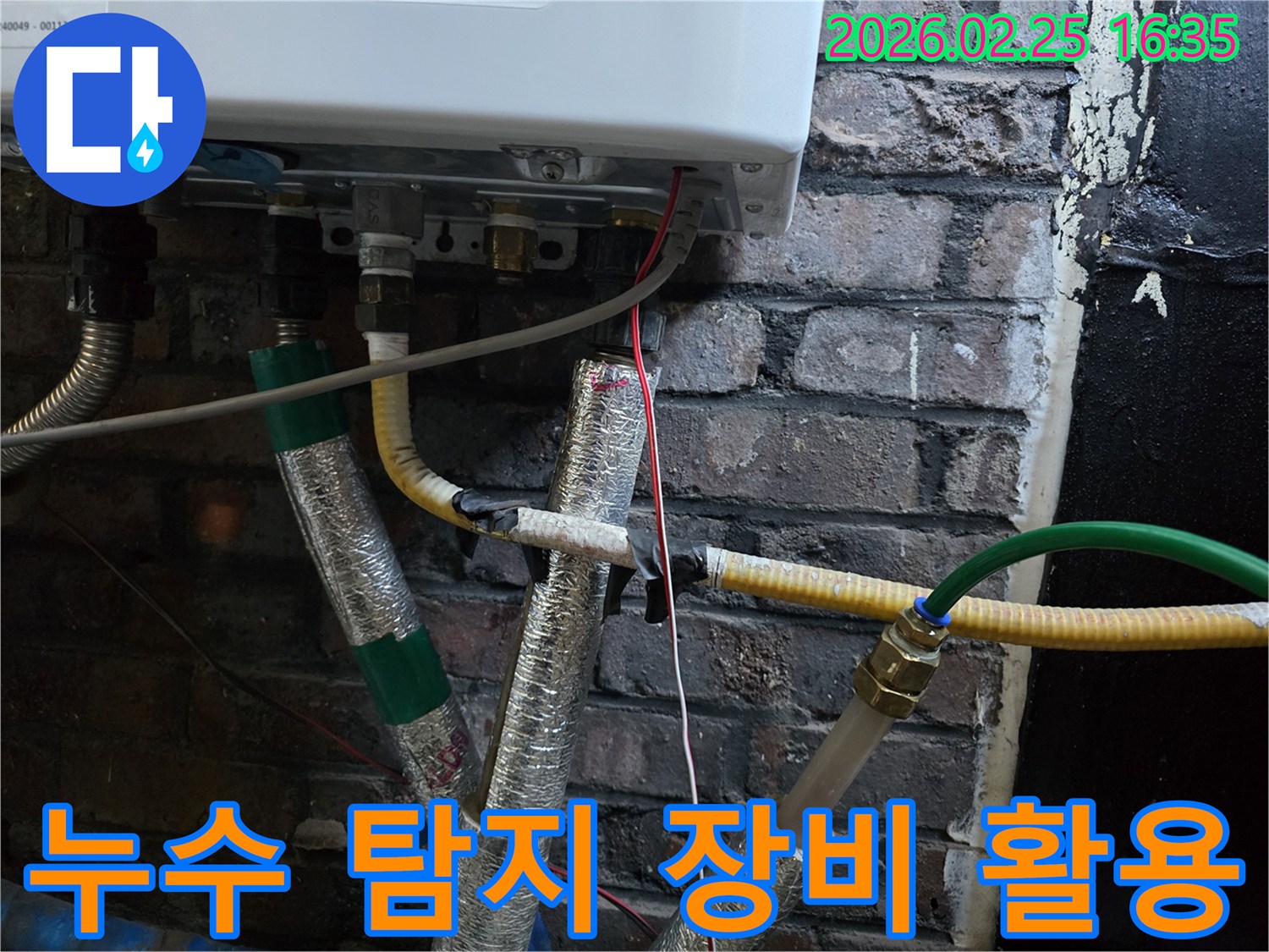 이 사진은-보일러 하부의-복잡한 배관들 사이에서-누수 탐지 장비를-활용하여-미세한 누수 지점을-찾아내는-전문가의-모습을-보여줍니다.