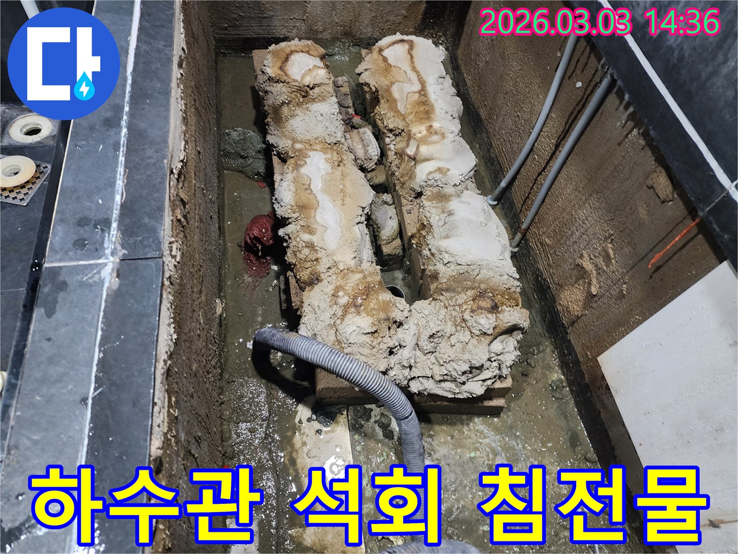 오래된 하수관 내부에 두껍게 쌓인 석회 침전물로 인해-배수 불량이 발생한 현장 사진입니다