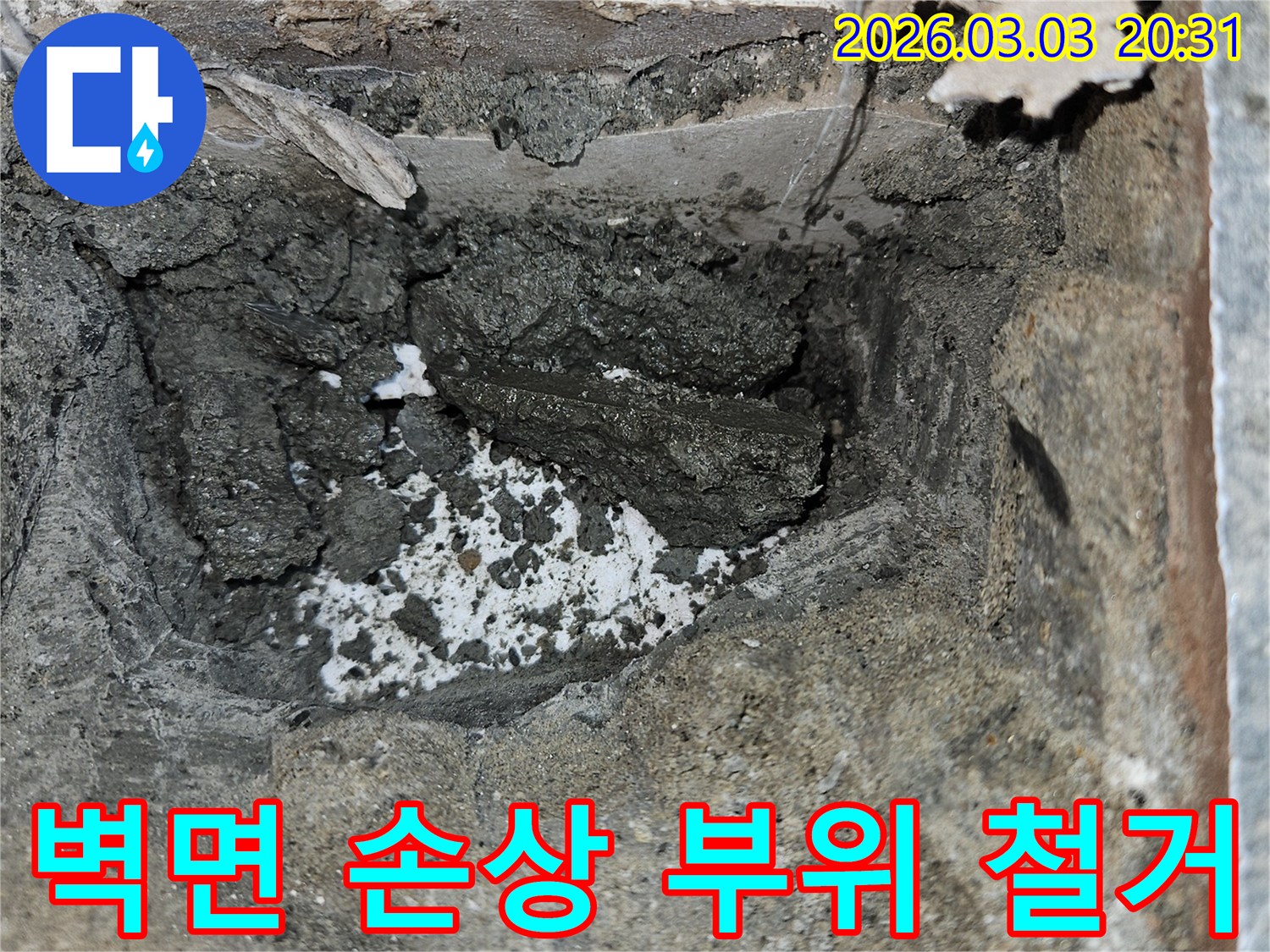 빌라 벽면 누수로 인해 손상된 부위를 철거하고 있습니다-내부의 젖은 시멘트와 부서진 잔해가 보입니다.