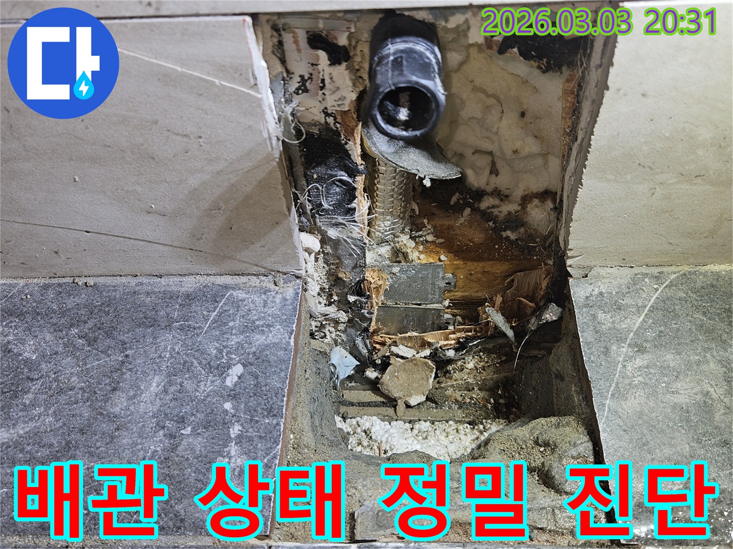 타일이 제거된 벽면 안쪽에서-누수 흔적과 함께 손상된 배관이 노출되어 정밀하게 진단 중인 모습