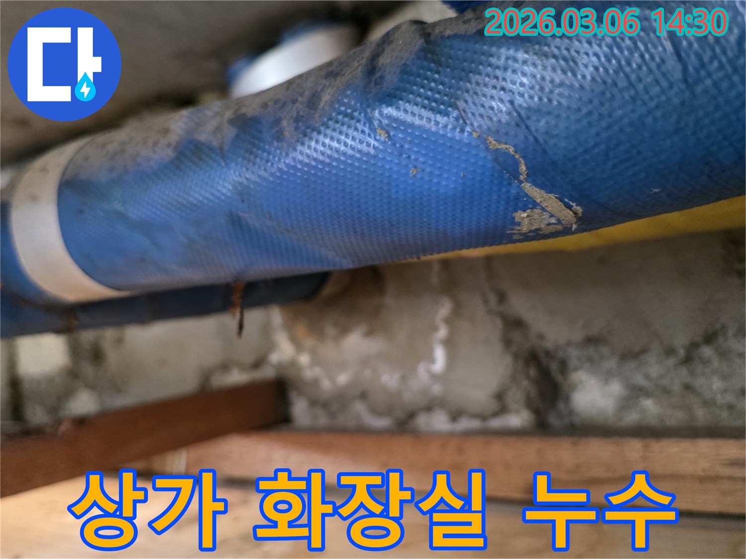 상가 화장실 내부-파란색 배관과-젖은 콘크리트 벽면-그리고 나무 지지대를-정밀하게 점검하는 모습