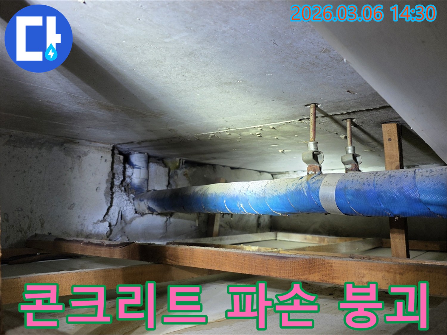지하 공간의 파란색 배관 옆-누수로 인해 파손되고-붕괴 위험이 있는 콘크리트 벽면을-누수 엔지니어가-점검하는 모습
