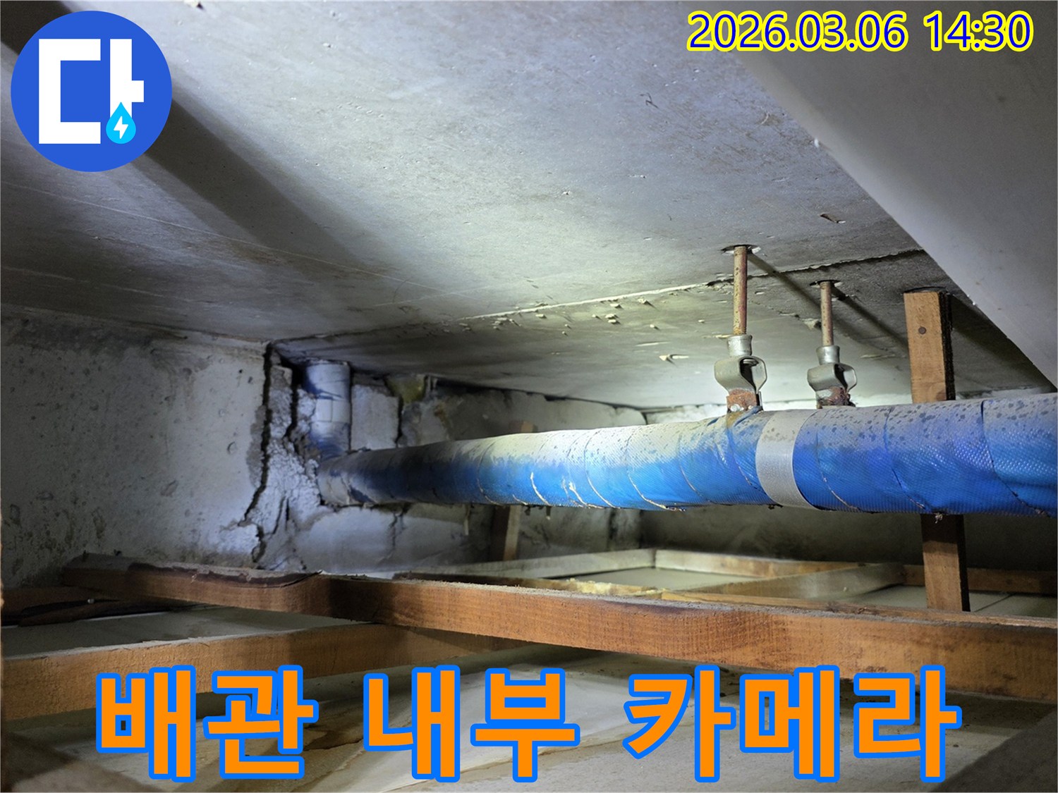 지하 공간의 파란색 배관과-손상된 콘크리트 벽면을-누수 엔지니어가-배관 내부 카메라 검사를-준비하는 모습