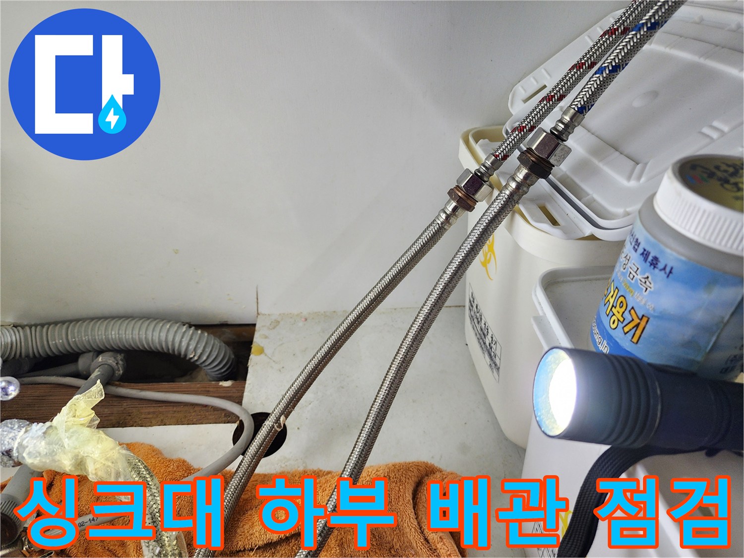 손전등으로 비춘 싱크대 아래쪽의 은색 고압 호스 및 연결 부위