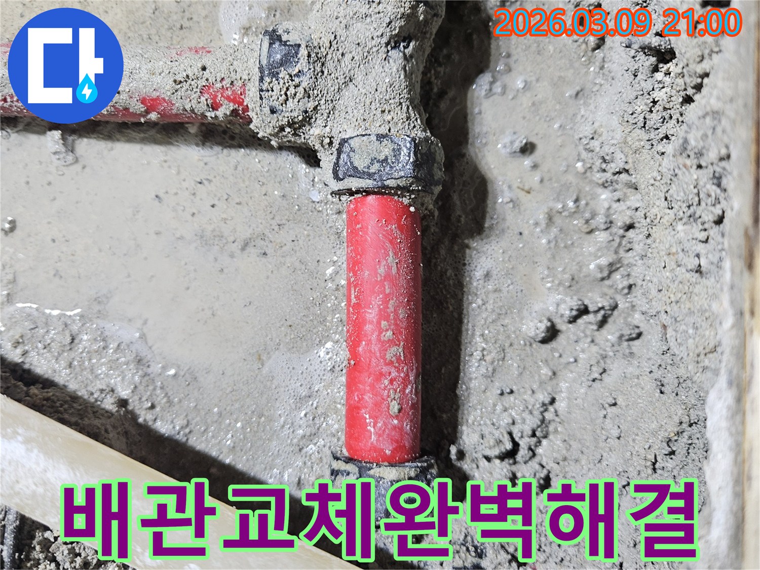 젖은 시멘트 바닥에-매립된 빨간색 배관의-손상된 부분을-새로운 배관으로-완벽하게 교체하여-누수를 해결한-모습입니다