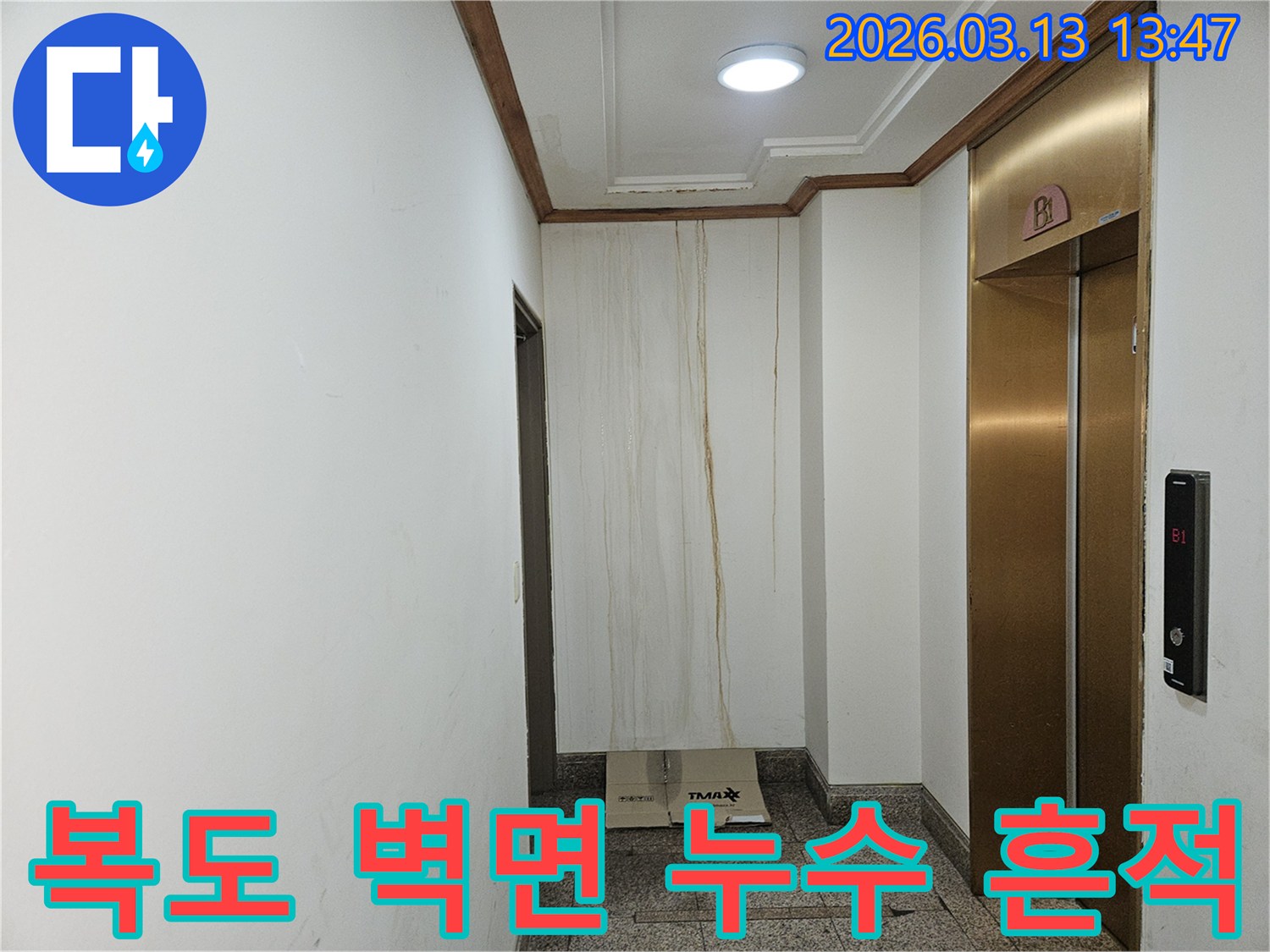 이 이미지는 아파트 복도 벽면에 발생한 심각한 누수 흔적을 보여줍니다-천장에서부터 아래로 길게 이어진 물자국이 명확하게 보입니다