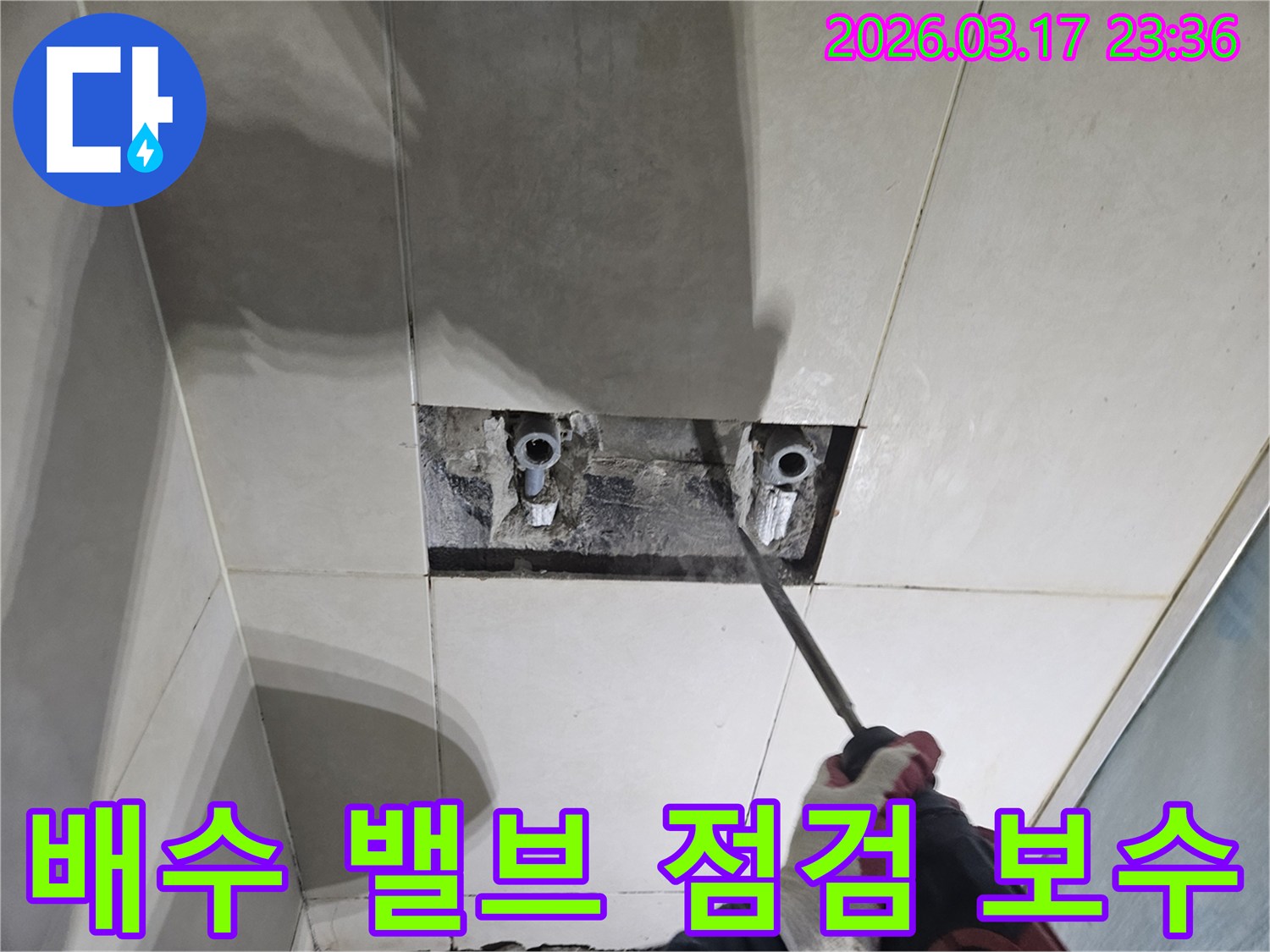 누수 지점을-찾기 위해-타일이 제거된-벽면에서-배수 배관의-역류 방지 밸브를-점검하는-모습입니다