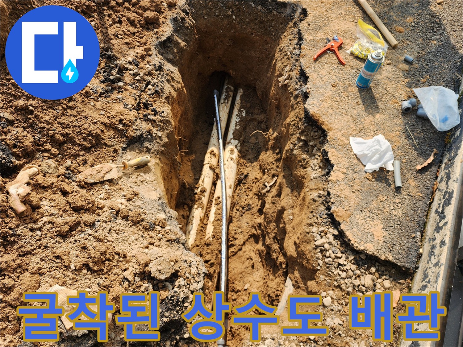 아스팔트 아래 드러난 손상된 수도 배관과 주변 작업 도구들