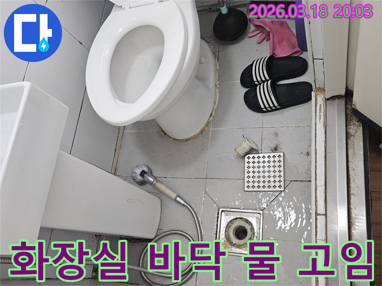오래된 화장실 바닥에-물이 고여있는-누수 현장을 담은-사진으로-변기와 샤워기-배수구가 보입니다
