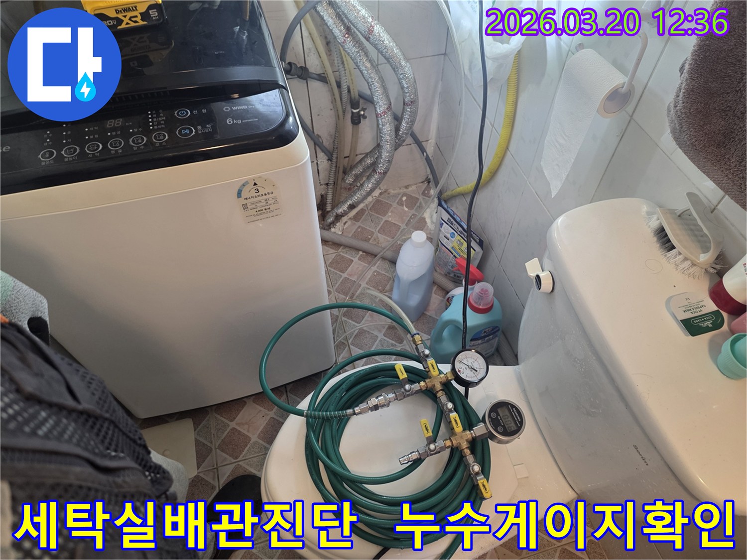 누수 엔지니어가 세탁기와 변기 사이 공간에서-배관 압력 검사 장비를 사용하여-누수 원인을 정밀하게 탐지하고 있습니다