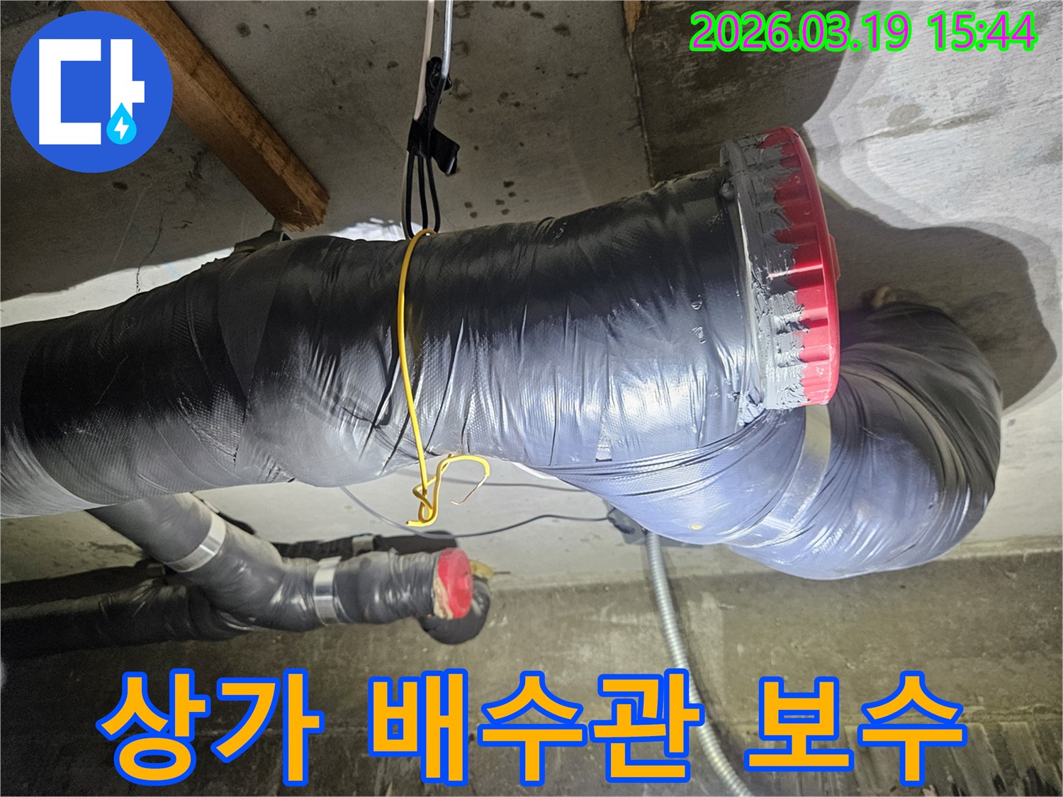 천장에 설치된 검은색 단열재로 감싸진 굵은 배수관과-그 옆으로 연결된 회색 파이프들이 보입니다