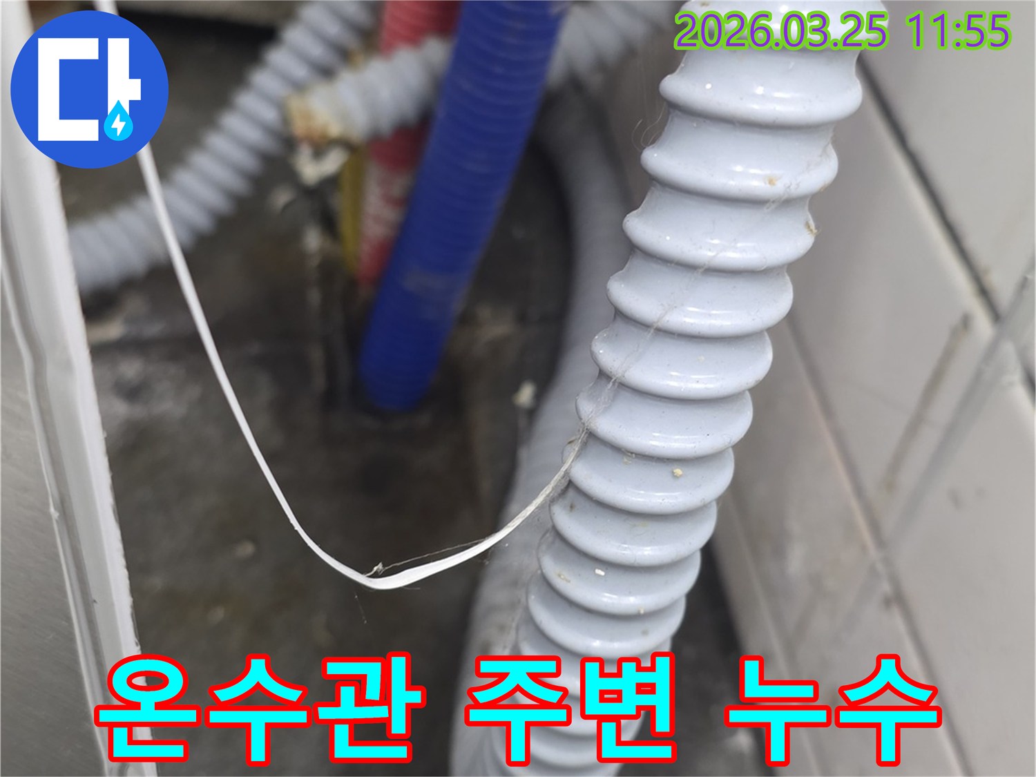 빨간색 온수관이-주름진 배수 호스 옆으로 지나가며-주변에 물기나 습기가-감지되는 모습으로-누수 가능성을 보여줌