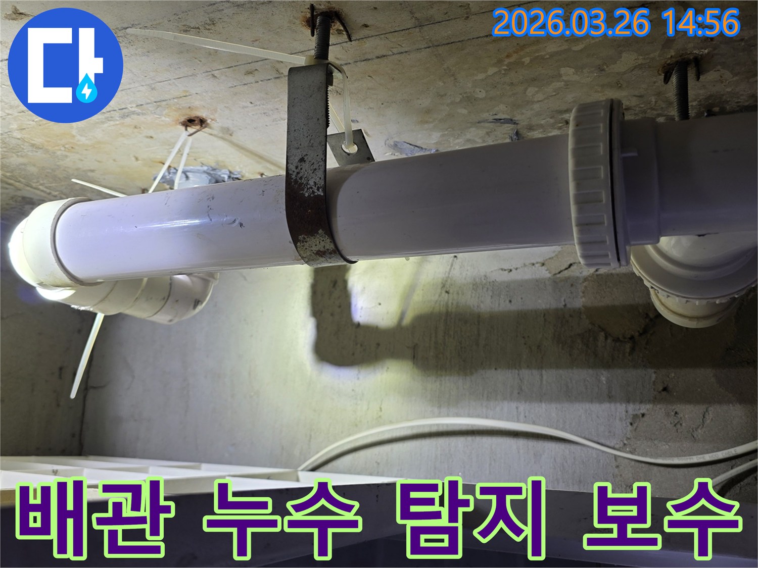 콘크리트 천장에 고정된-하얀색 배관의 연결 부위와-녹슨 지지대를 점검하는 모습으로-누수 탐지 및 보수 과정을 보여줍니다