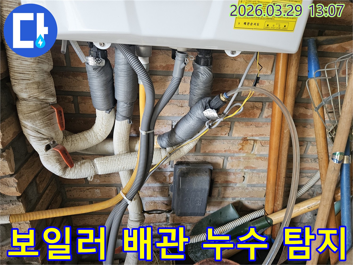 이 이미지는 벽돌 벽에 설치된 보일러 배관의 누수 탐지 작업을 보여줍니다-회색 단열재로 감싸진 파이프들이 복잡하게 연결되어 있습니다.