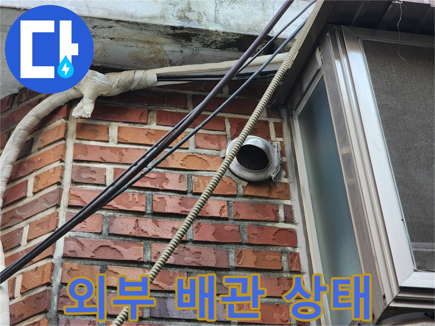 붉은 벽돌 외벽에 고정된 배관과 환기구 근처 사진입니다.