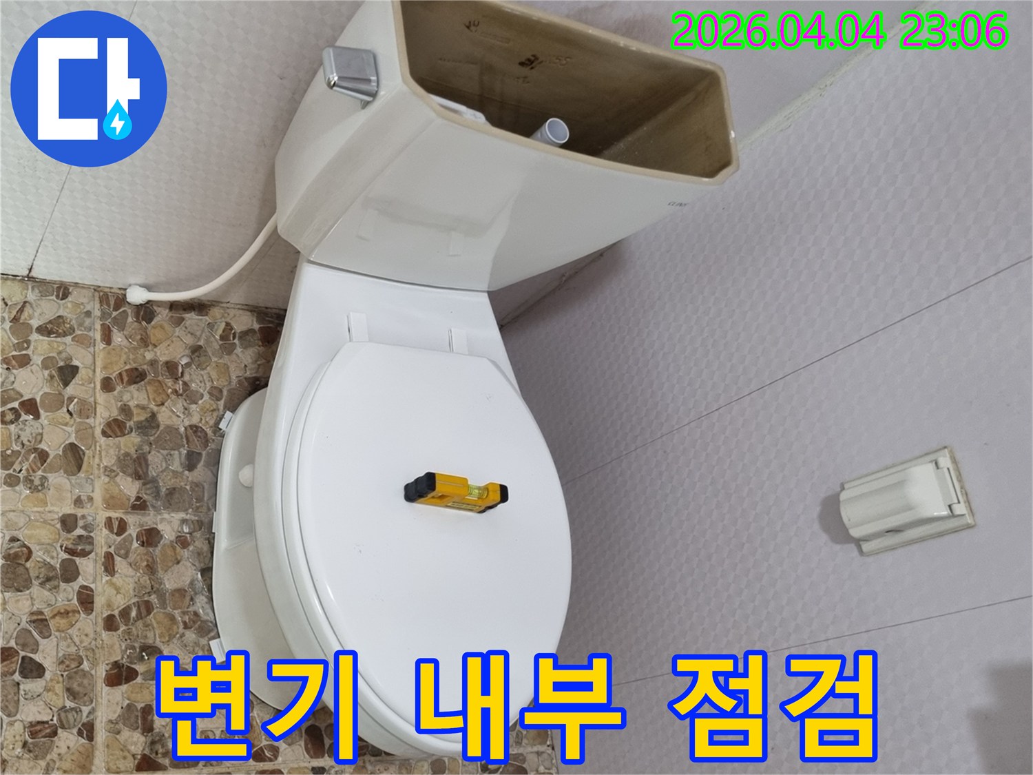 변기 물탱크 덮개가 제거된 상태로-내부 부품이 선명하게 보이며-수평계가 변기 시트 위에 놓여 있습니다