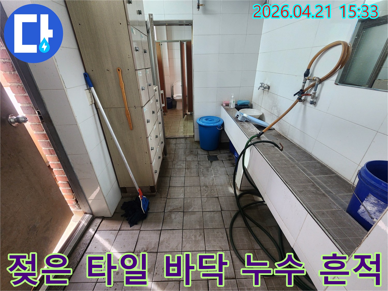 물에 젖어 얼룩진 타일 바닥과-주변의 사물함-수도 시설이 보이는 누수 현장