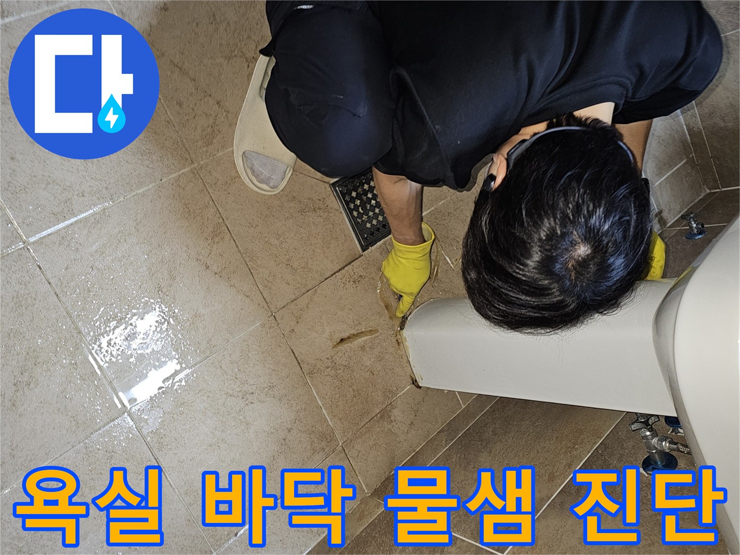 누수 엔지니어가-노란색 장갑을 착용하고-욕실 바닥의 젖은 부분을-손가락으로 가리키며-누수 원인을 면밀히 파악하고 있습니다