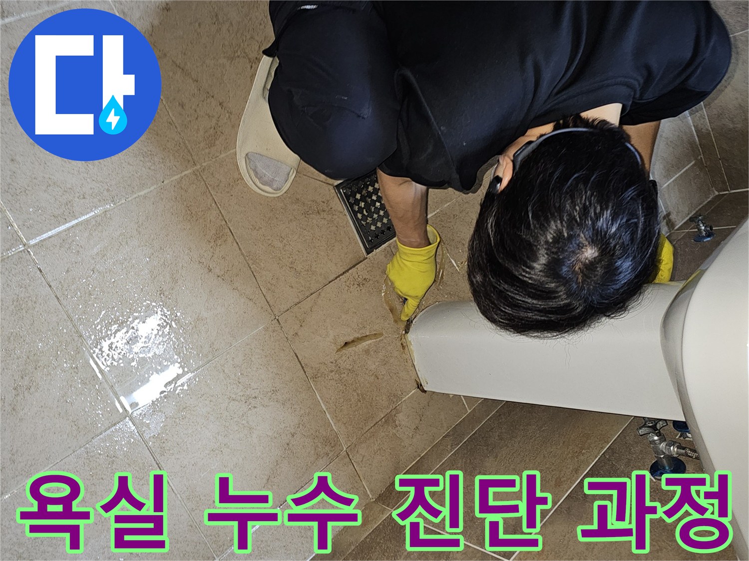 누수 전문가가-노란 장갑을 끼고-욕실 바닥의 젖은 타일과-세면대 하단부를-집중적으로 관찰하며-누수 지점을 파악하고 있습니다