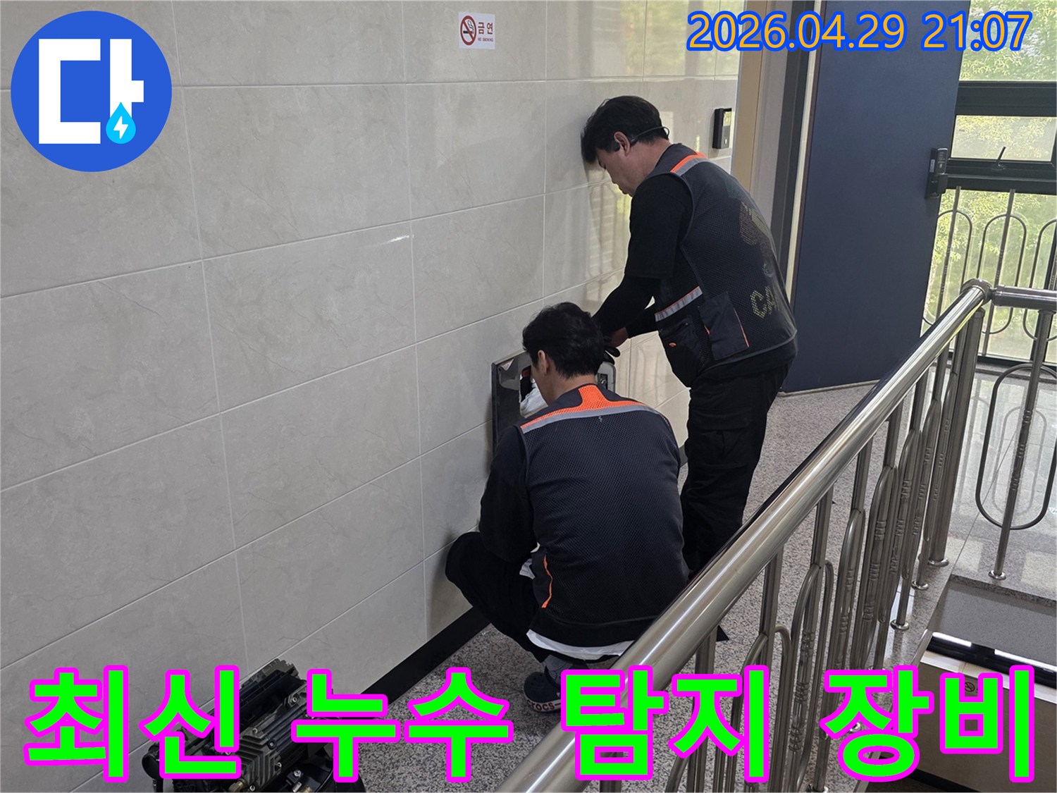 두 명의 전문 기술자가 최신 누수 탐지 장비를 사용하여 건물 벽면의 누수 의심 지점을 정밀하게 탐지하고 있습니다-정확하고 효율적인 문제 해결을 위한 필수 도구입니다.
