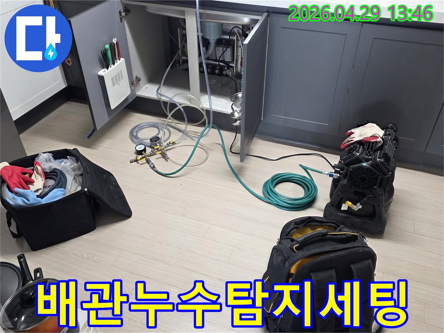 싱크대 하부 공간에-누수 탐지를 위한-압력 게이지와-연결 호스-그리고 공기 압축 장비를-설치하고 있는 장면입니다