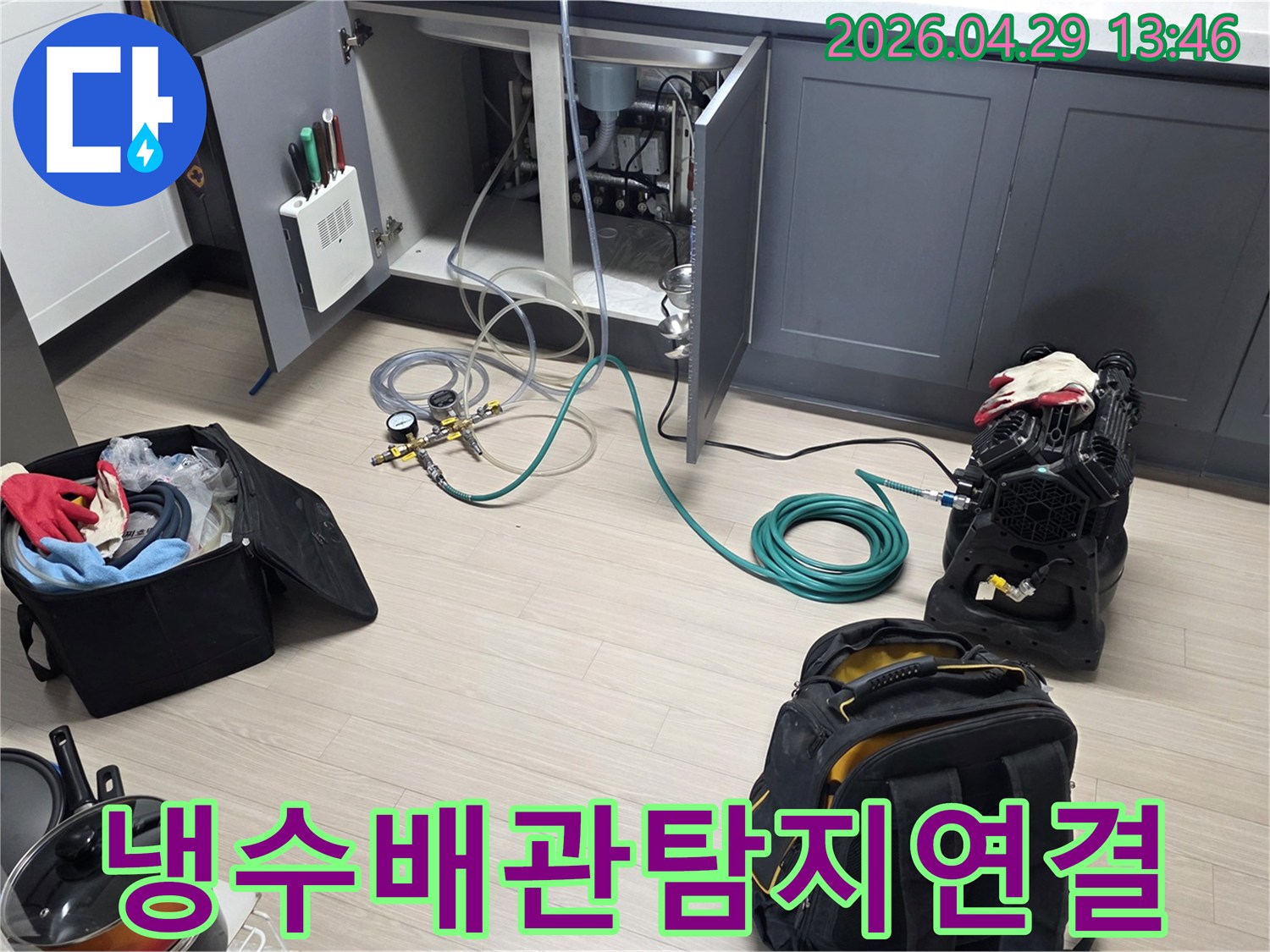 아파트 주방 싱크대 하부에서-냉수 배관의 누수를 확인하기 위해-압력 게이지와 호스-그리고 공기 압축 장비를-연결하는 작업이 진행 중입니다