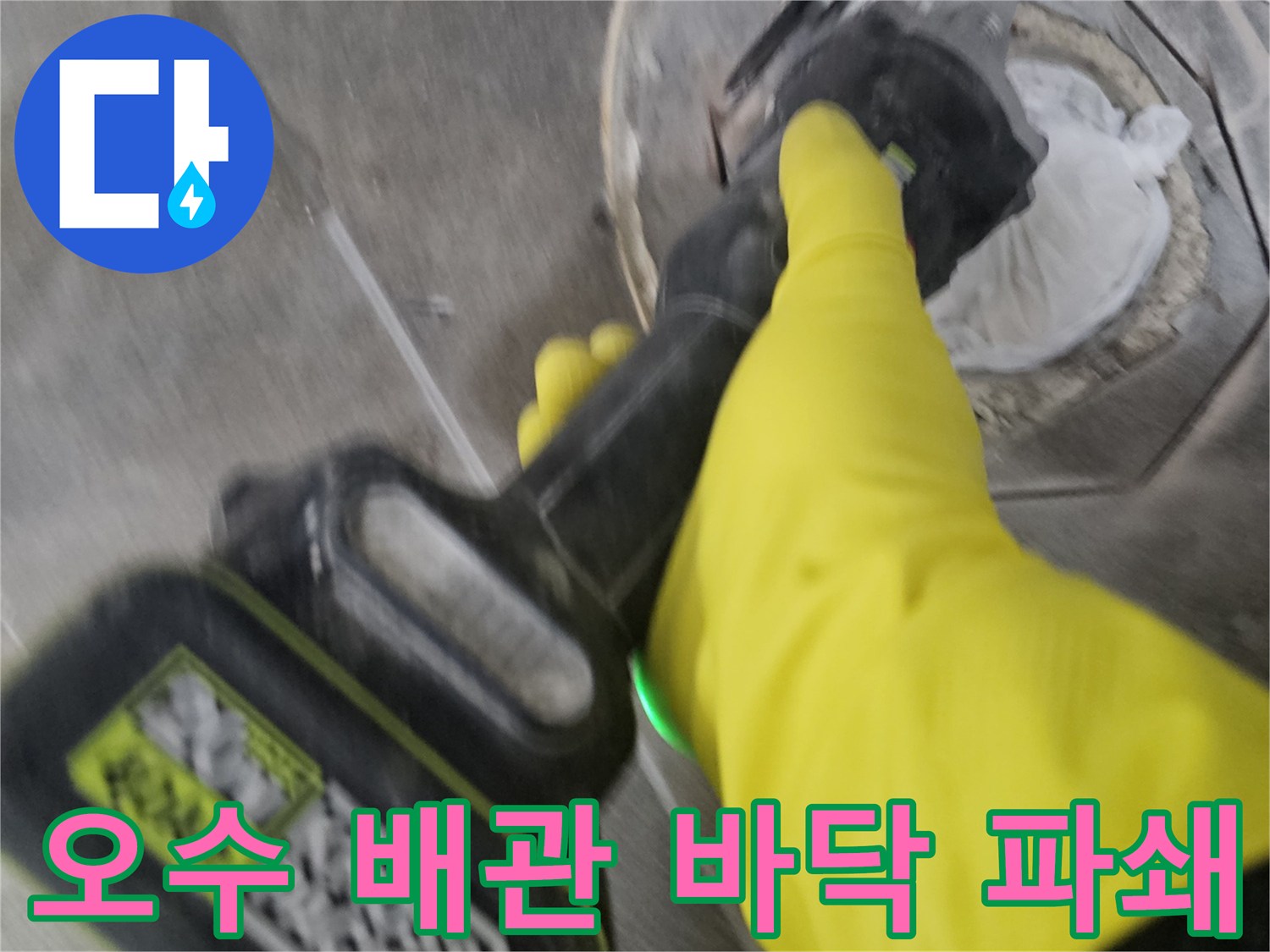 노란색 보호 장갑을 착용한-작업자가-전동 공구를 이용해-오수 배관 주변의-굳은 타일을-조심스럽게 파쇄하는 모습입니다.