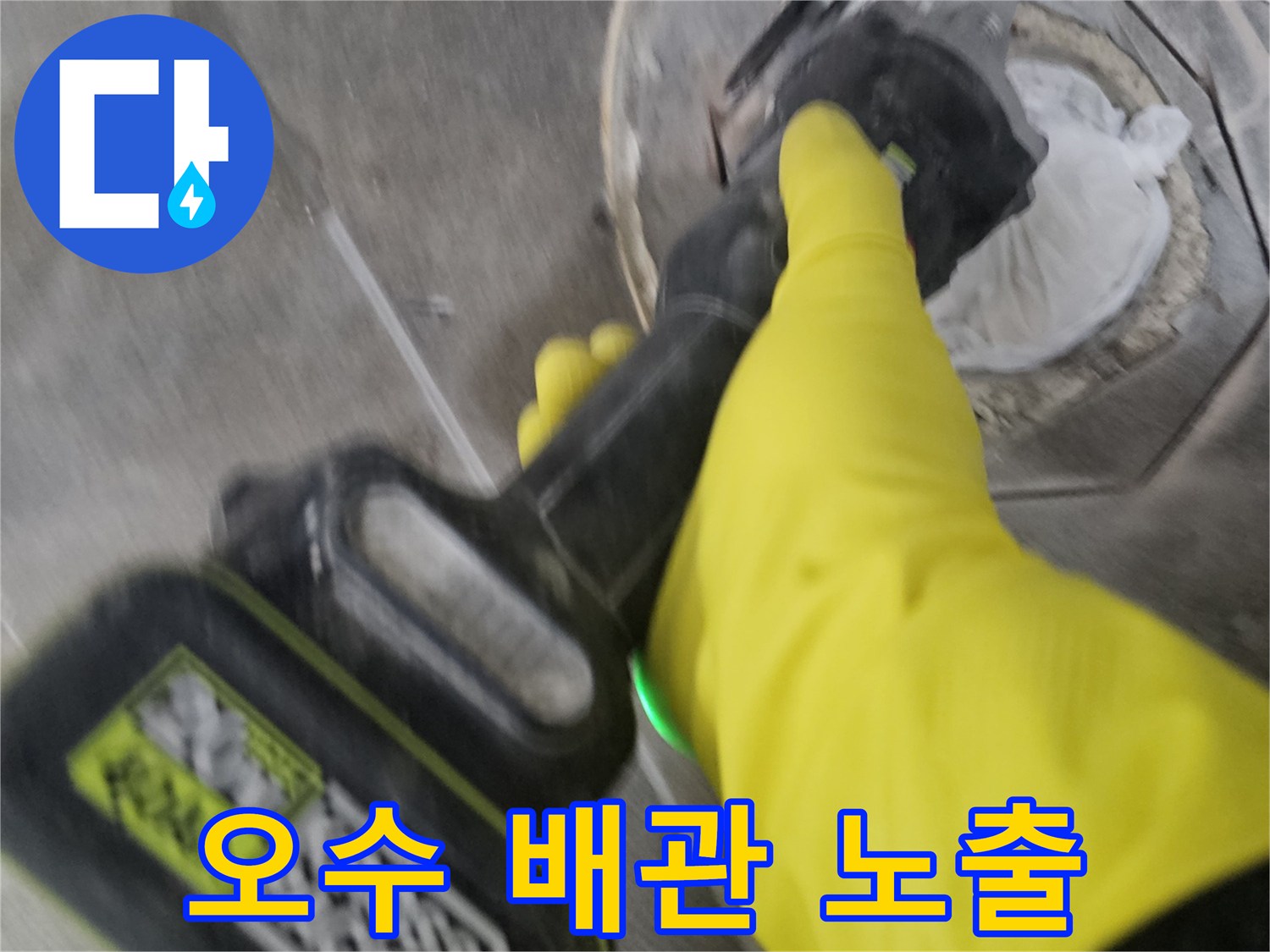 노란색 안전 장갑을 착용한-기술자가-전동 공구를 사용하여-오수 배관 주변의 바닥 타일을-정교하게 제거하여-배관을 노출시키는 현장입니다.