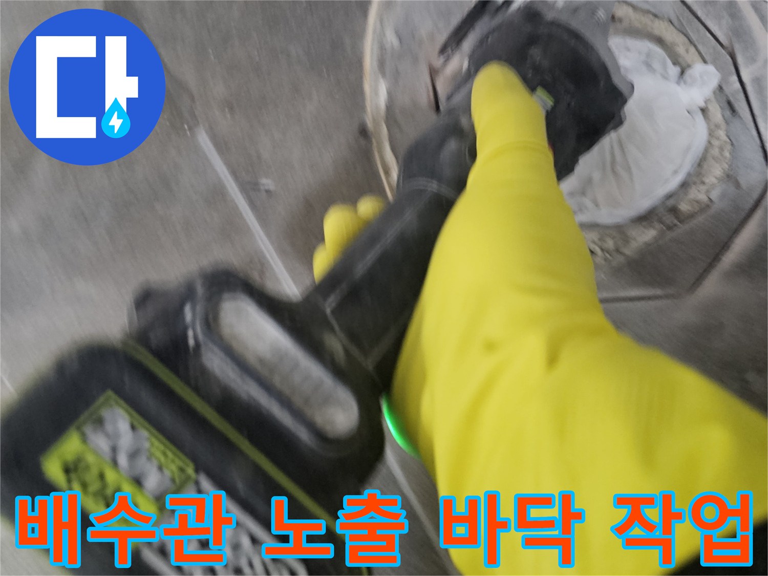 노란색 작업 장갑을 착용한-전문가가-전동 공구로-배수관 주변의 바닥 타일을-세심하게 제거하여-배수관을 노출시키는 과정입니다.