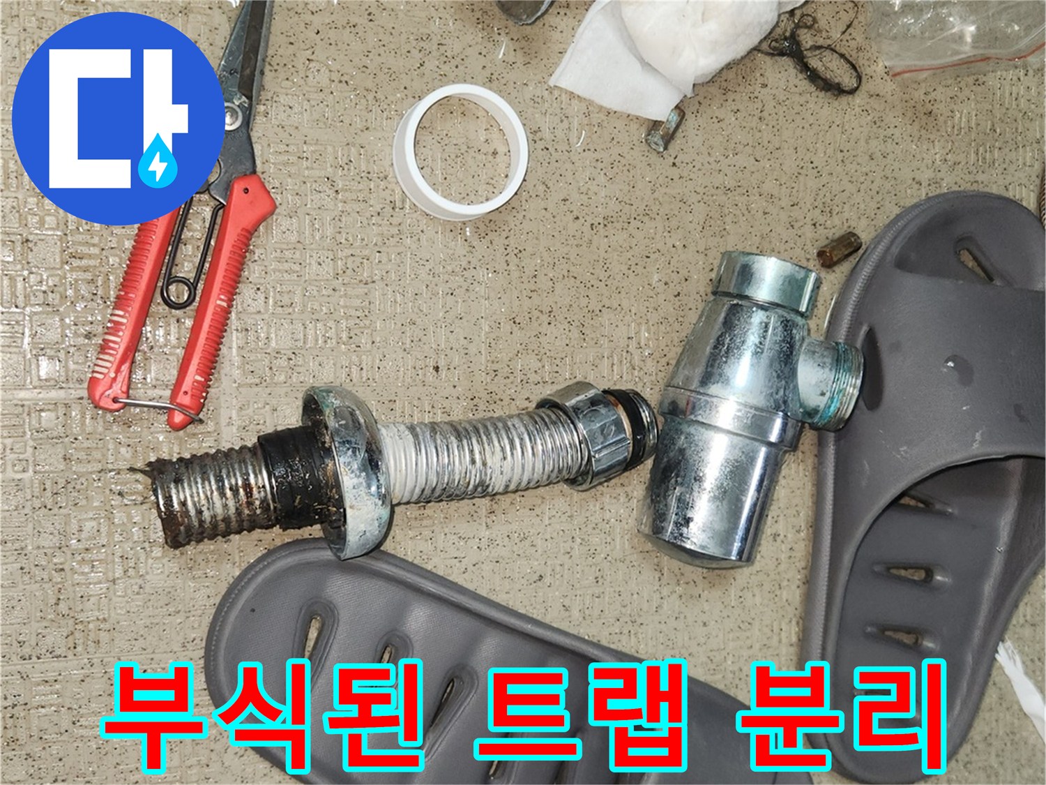 수명이 다한 배수 트랩의 부품들이 바닥에 놓여있으며-새로운 트랩으로 교체될 예정입니다