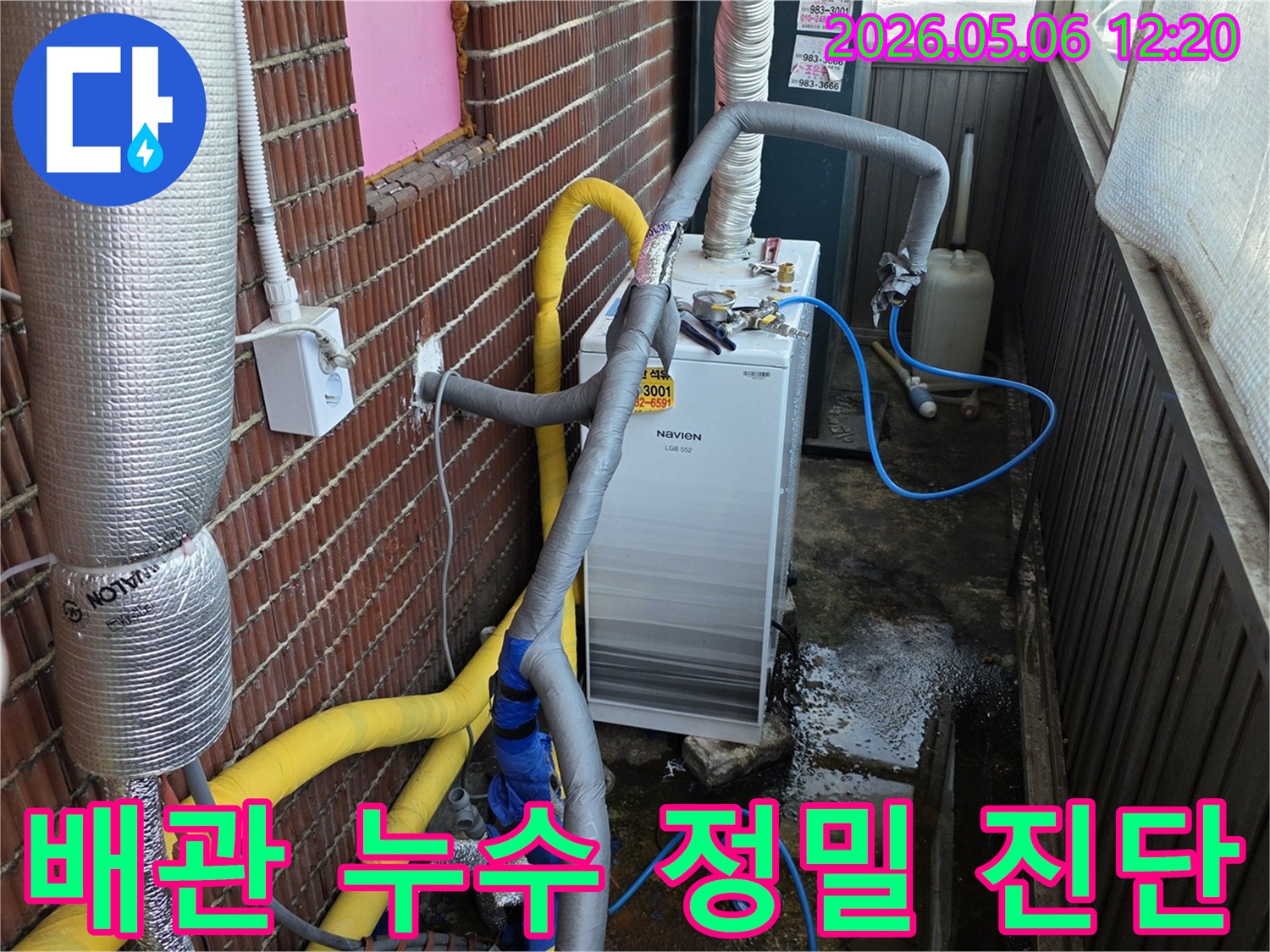 누수 지점을 찾기 위해-배관에 연결된 파란색 호스와-주변에 고인 물이 보이는-보일러실 작업 현장입니다