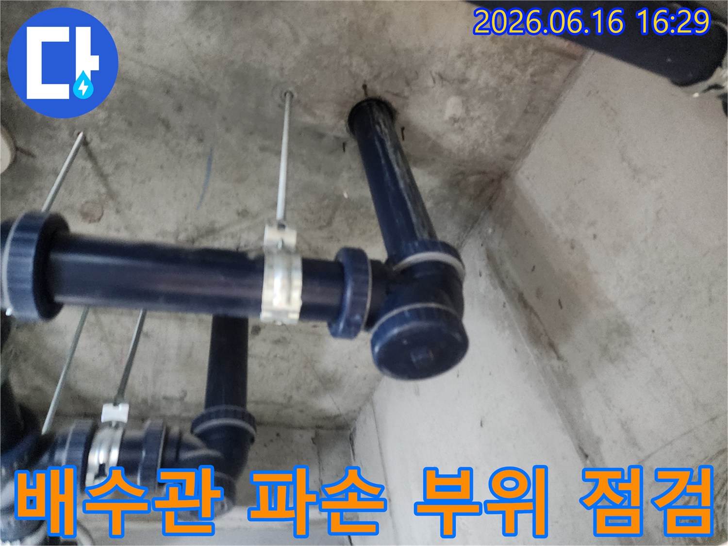 콘크리트 천장에 고정된 어두운 색 배수관의-연결 부위를 자세히 살펴보는 모습입니다.