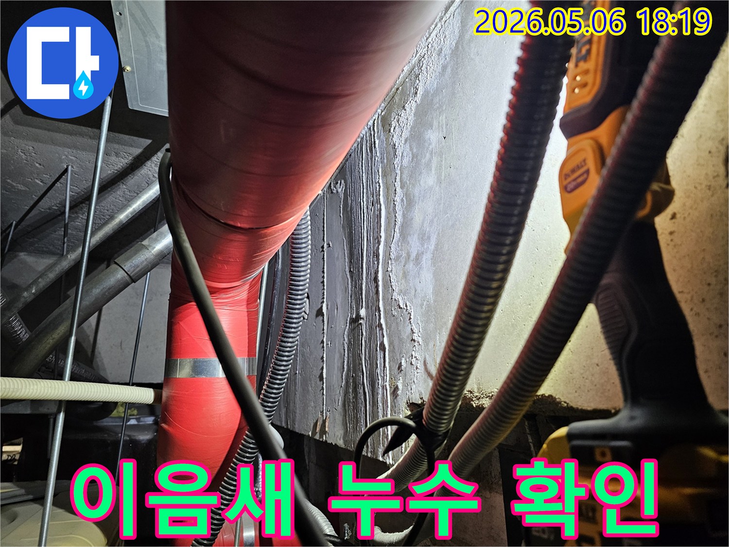 어두운 지하 공간에서-빨간색 단열 배관의-이음새 부위와-그 주변-젖은 벽면을-집중적으로-점검하며-누수 여부를-확인하는-모습